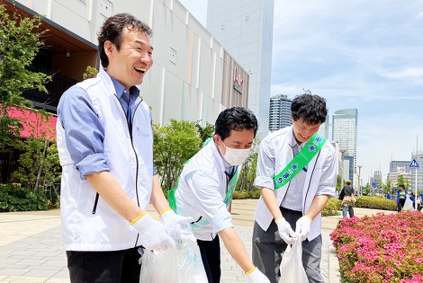 たすきを掛けた従業員が、歩道でごみを拾っている様子