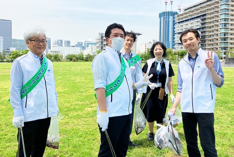 清掃活動を終えた参加者が、ごみ袋を手に芝生広場に並んでいる様子