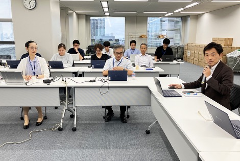 会議室に集まった従業員が、正面の画面を見ながら会議に参加している様子